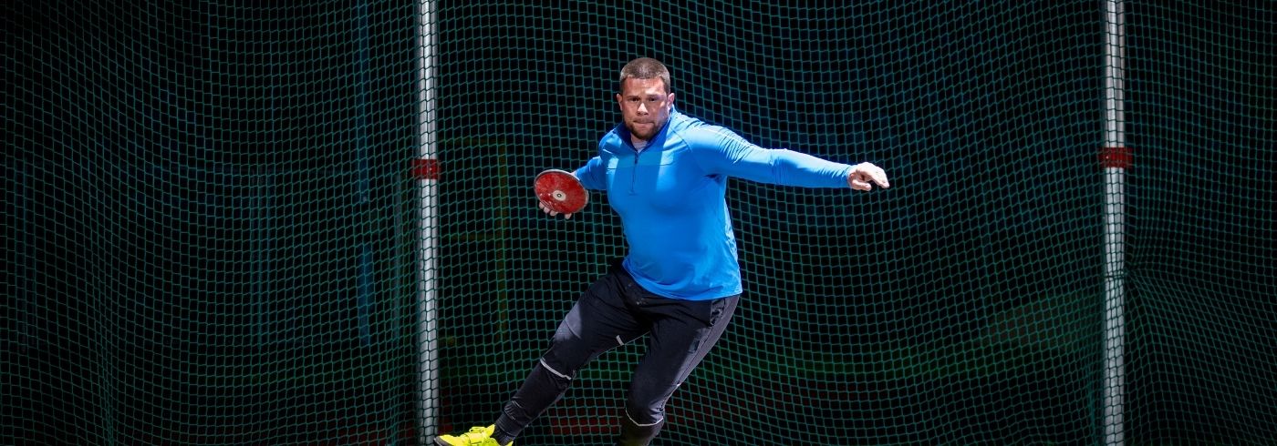 man throwing red discus from a cage