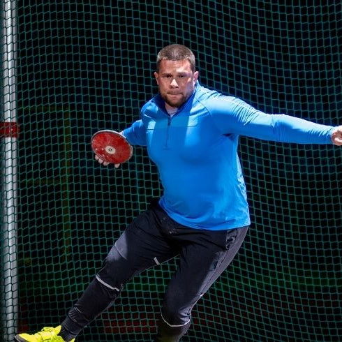 man throwing red discus from a cage