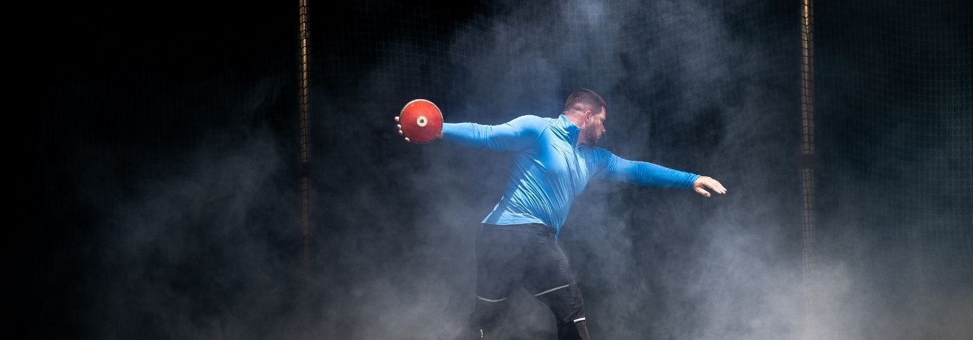 man with red discus in a throwing cage