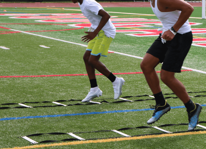 Athletes using agility footwork ladders on a grass pitch
