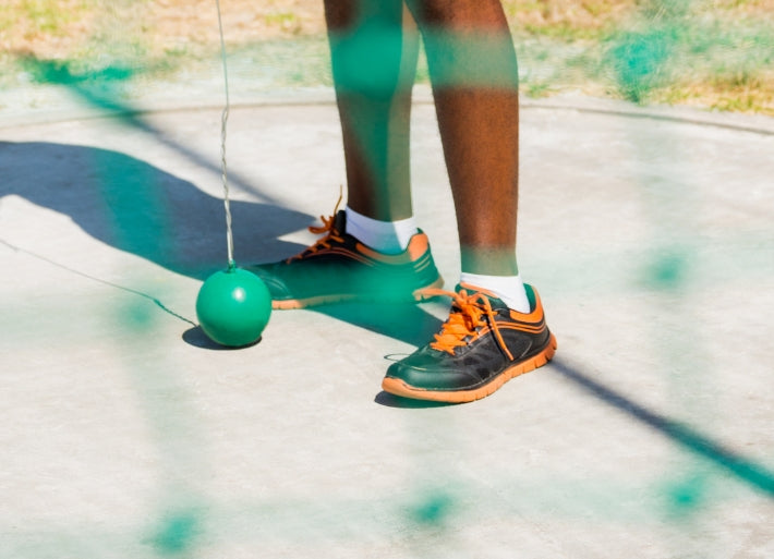 Legs of a hammer thrower shown through the cage net, standing in the hammer circle with a hammer. 