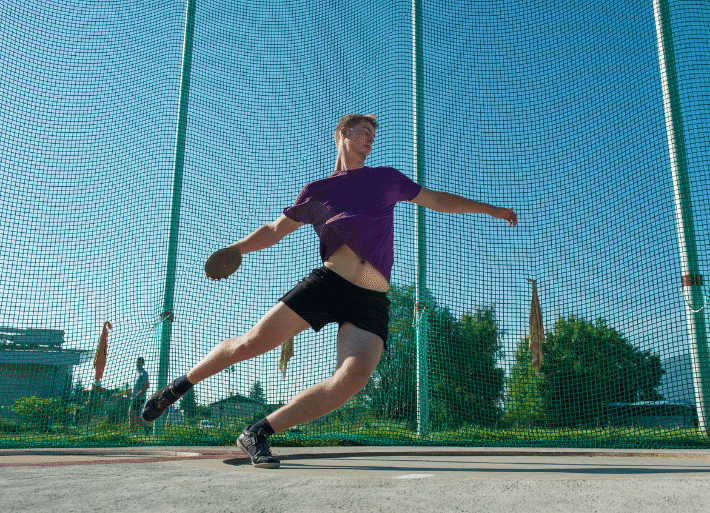 Athlete throwing discus in throwing circle with safety net cage