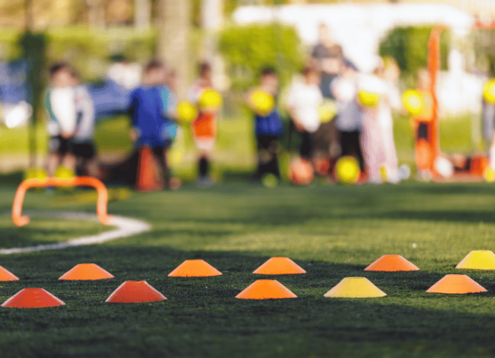 School sports equipment laid out on a grass field with children in the background