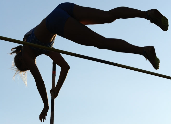 Pole vaulter clearing the bar in shadow against a blue sky