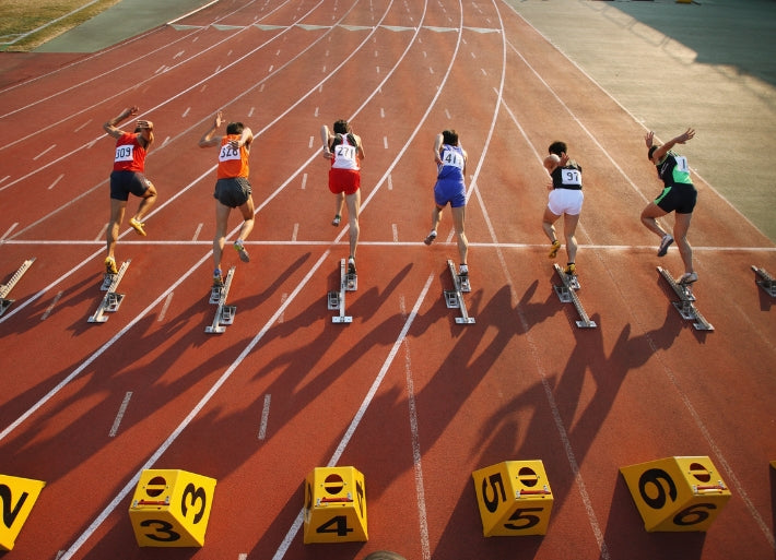 Row of sprinters coming out of blocks at the start of a 100m race