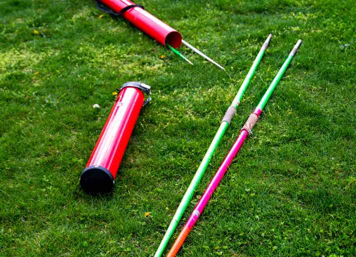 Two athletics javelins lying on grass next to a hard red javelin case tube