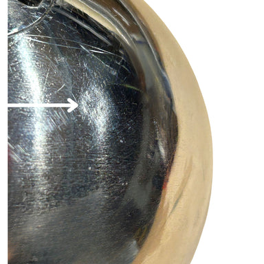 Close-up of a stainless steel hammer surface with visible scratches and a white arrow pointing to a damaged area, against a light neutral background.