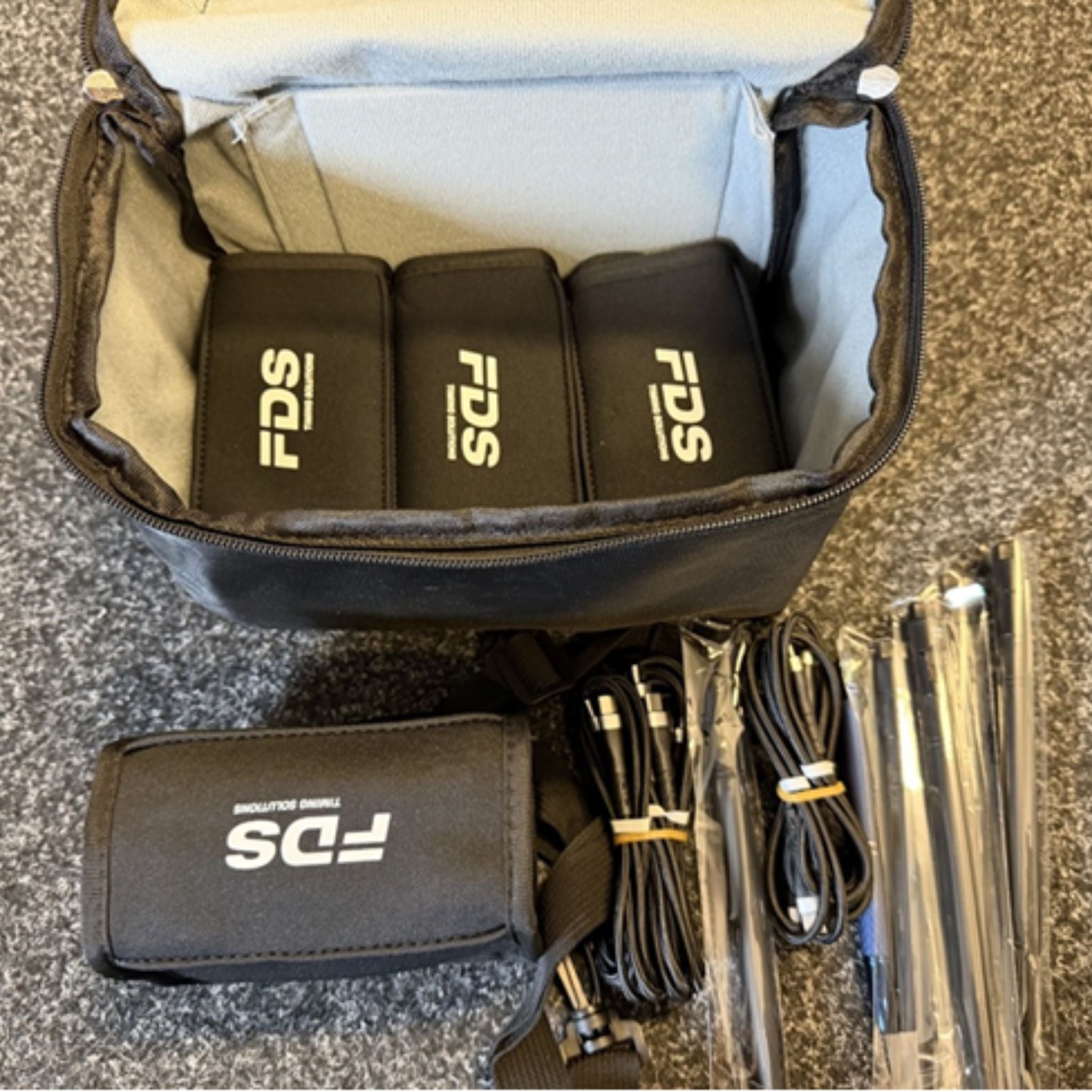 Open bag containing FDS branded neoprene cases for photocells and timing device, with USB cables on a textured surface