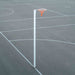 A freestanding white pole with an orange net and white hoop, set on a dark asphalt court with white painted lines.