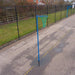 A blue socketed netball hoop with a green net on an outdoor paved court, with a chain-link fence and grass in the background.