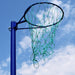 A green netball net attached to a blue hoop and support pole, photographed outdoors against a blue sky with white clouds.