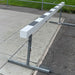 White wooden steeplechase barrier with metal adjustable legs on a concrete surface with grass in the background